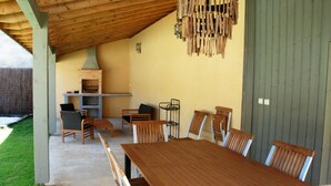Un porche cubierto con una mesa y sillas de madera, una parrilla y un colgador de luz.