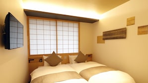 A neatly made bed with a headboard, a wall-mounted TV, and a window with a grid pattern. - Stay SAKURA Kyoto SUZAKU OJI (Kyoto)