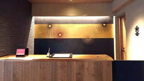 A reception desk with a wooden finish, a black and gold decorative wall, and a sign that reads "Check Out". - Stay SAKURA Kyoto SUZAKU OJI (Kyoto)