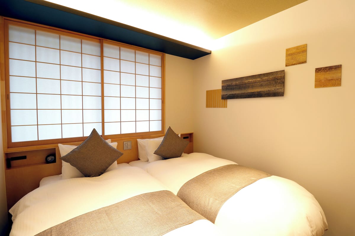 Ein Hotelzimmer mit großem Fenster, einem Bett mit vielen Kissen und an der Wand befestigter Kunst.