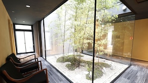 A waiting area with a glass wall, wooden chairs, and a small indoor garden. - Stay SAKURA Kyoto SUZAKU OJI (Kyoto)