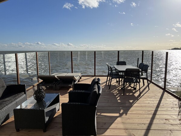 Eine Terrasse mit Korbmöbeln, einem Tisch und Stühlen mit Blick auf ein Gewässer.