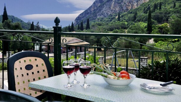 Una mesa con ensalada y copas de vino en un balcón con vistas a un paisaje montañoso.