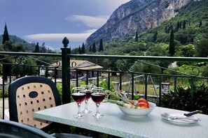 A table with a bowl of salad and wine glasses on a balcony overlooking a mountainous landscape.