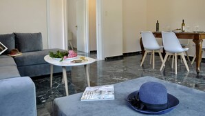 Una sala de estar moderna con un sofá gris, una mesa de centro redonda con una revista y un sombrero azul sobre un reposapiés gris.