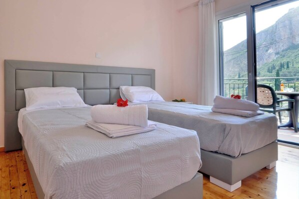 A hotel room with two beds, a balcony with a mountain view, and a table with a bottle.