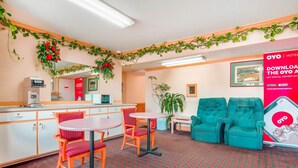 A hotel lobby with a reception desk, two round tables with chairs, a green sofa, and a patterned carpet. - OYO Hotel Durham West Hills (Durham)
