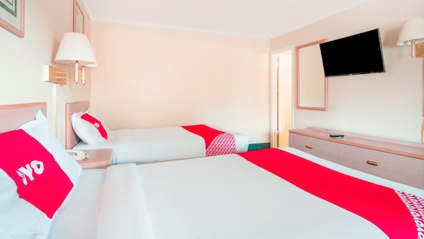 A hotel room with two beds, a TV, a desk, and a mirror. - OYO Hotel Durham West Hills (Durham)