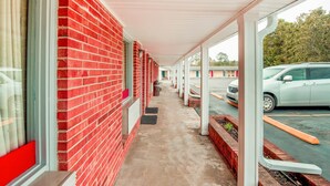 A covered walkway with red brick walls and a concrete floor, leading to a parking area with cars. - OYO Hotel Durham West Hills (Durham)