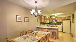 Comedor con mesa de madera dispuesta para cuatro personas, cocina al fondo y una araña.