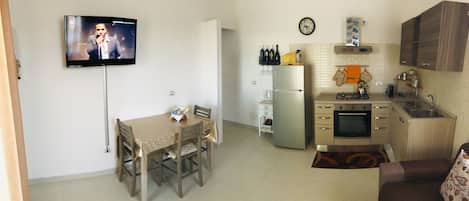 Un espacio habitable compacto con comedor, kitchenette y televisor montado en la pared.