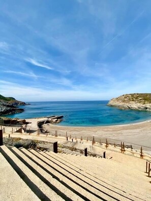 A coastal view with a beach, rocky outcrops, and a clear sky.