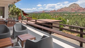 Une terrasse dotée de tables et de chaises en bois, offrant une vue sur un paysage montagneux sous un ciel dégagé.