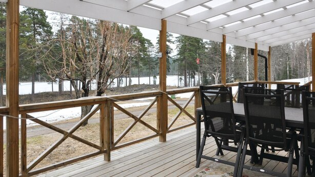A covered outdoor area with a wooden deck, metal chairs, and a view of a lake surrounded by trees. - 2 bedroom gorgeous home in Gunnarskog (Gunnarskog)