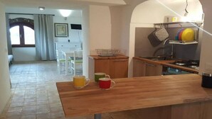 Une cuisine compacte avec un plan de travail en bois, un évier et une cuisinière. On y trouve deux chaises et une table à manger dans l’espace repas adjacent.