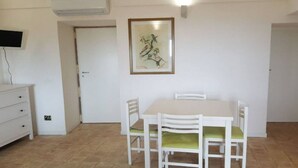 Un coin repas avec une table et des chaises blanches, une œuvre d’art encadrée au mur et une commode blanche avec des tiroirs.