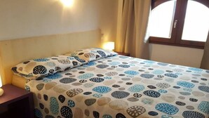 Un lit avec une couvre-lit à motifs et des oreillers, une table de chevet et une fenêtre avec des rideaux.