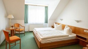 Une chambre individuelle comprenant un lit, une chaise, une petite table et une fenêtre avec des rideaux.