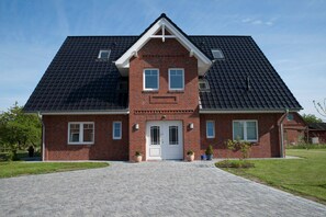 Une maison à deux étages, construite en briques, avec une façade symétrique, une entrée centrale et une allée pavée.