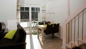 Una sala de estar con un sofá, una mesa de comedor con sillas, una escalera y vistas al exterior a través de una puerta de vidrio.