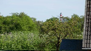 Un balcón con una mesa y una planta en maceta, con vistas a un jardín y un edificio con una estructura roja y blanca a lo lejos.