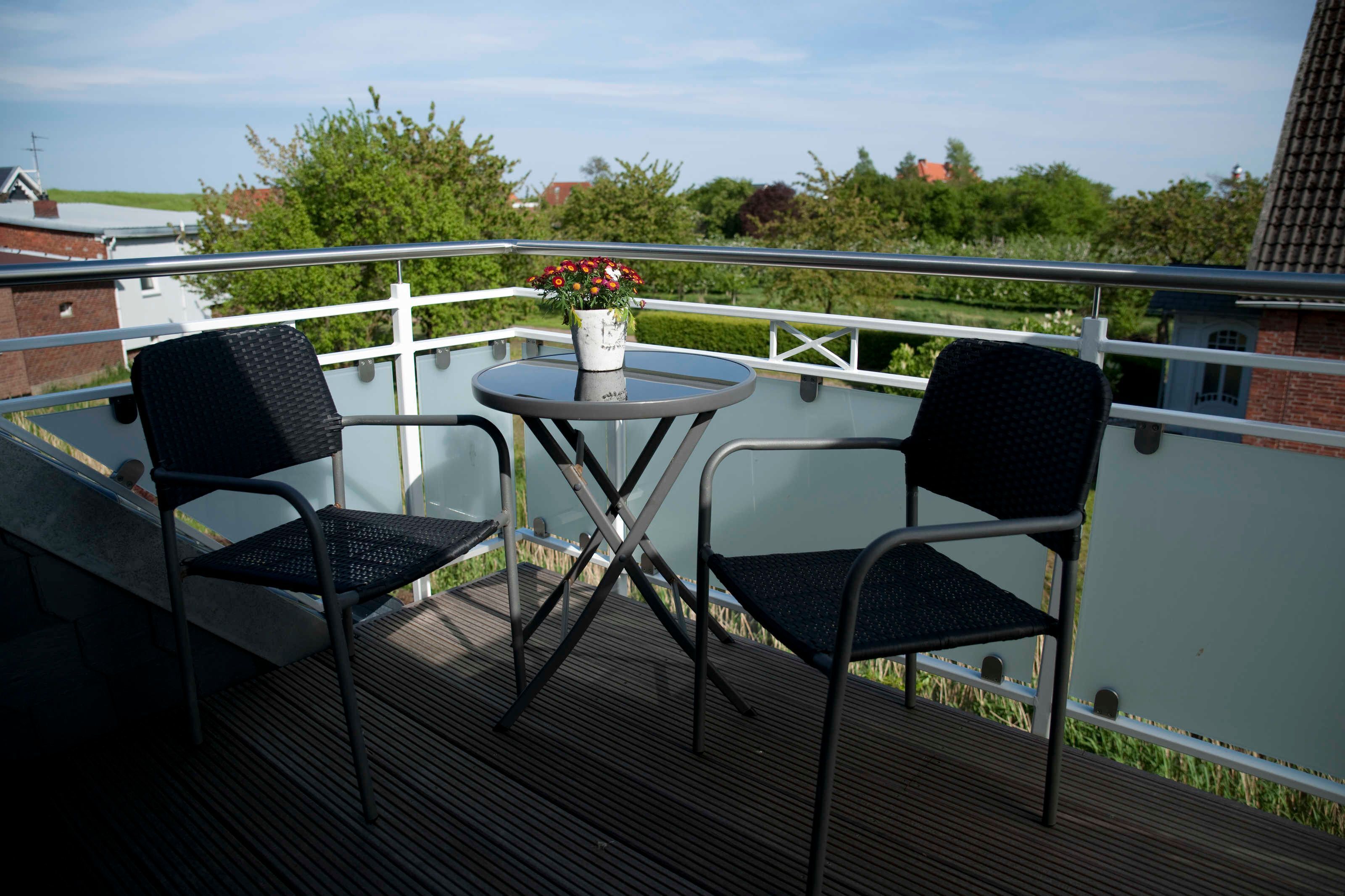Een balkon met twee stoelen, een klein rond tafeltje en een bloempot.