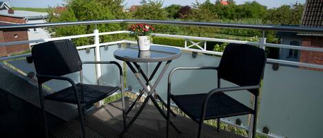 Een balkon met twee stoelen, een klein rond tafeltje en een bloempot.
