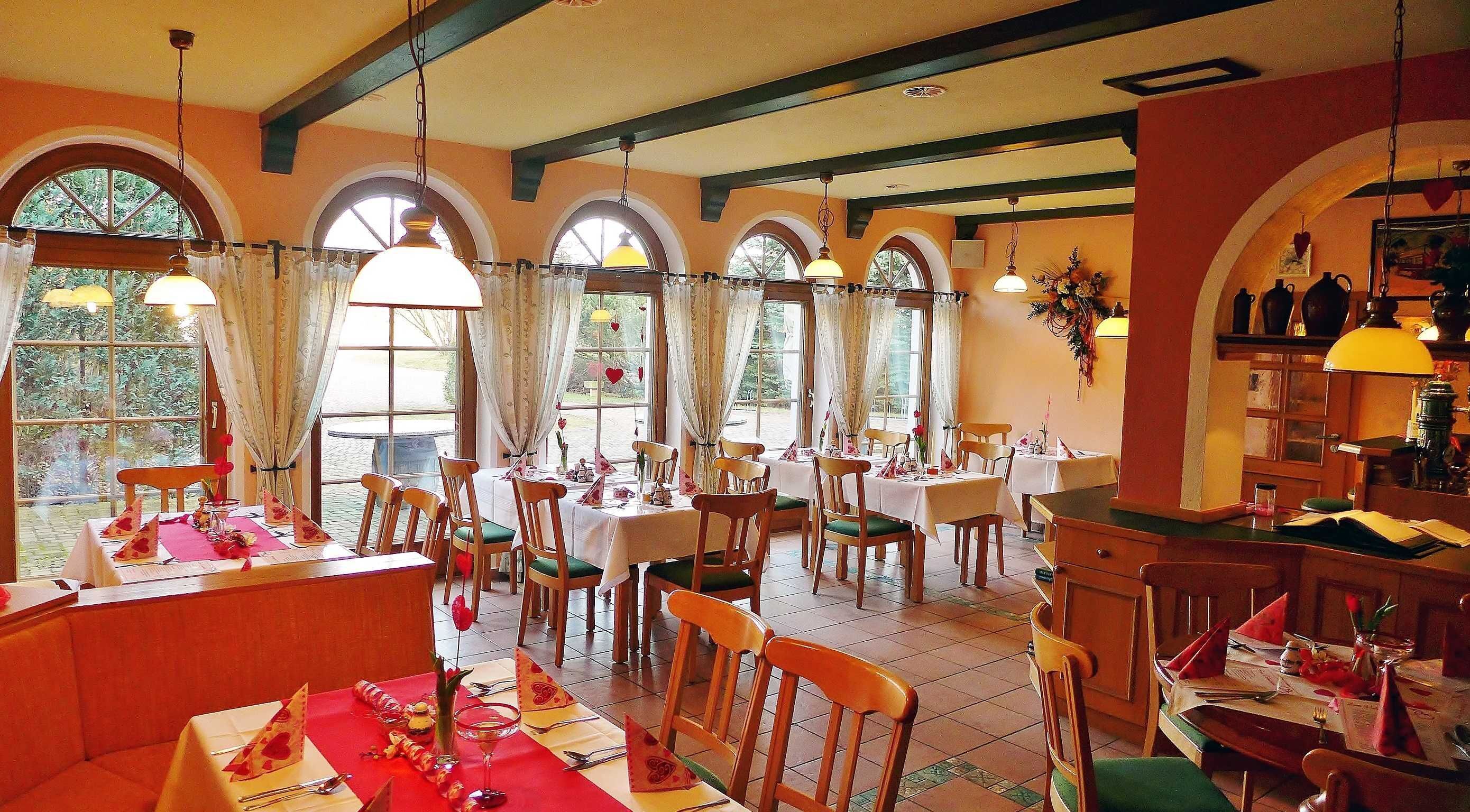 Un restaurant avec de nombreuses tables, des chaises en bois et de grandes fenêtres dotées de rideaux.