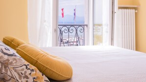 Ein Schlafzimmer mit einem Bett, Kissen und Blick auf einen Balkon mit Geländer und einer Flagge.