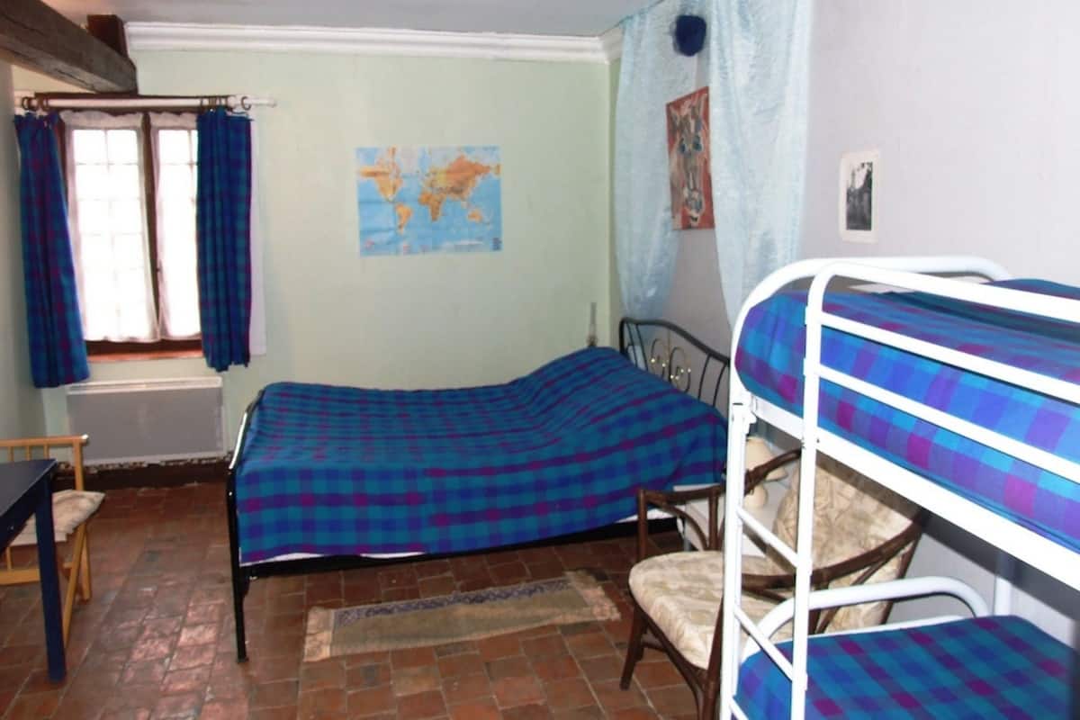 A room with a bed, a chair, a map on the wall, and a window with curtains.