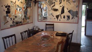 Uma sala de jantar com uma mesa grande coberta por uma toalha estampada, cercada por cadeiras de madeira.
