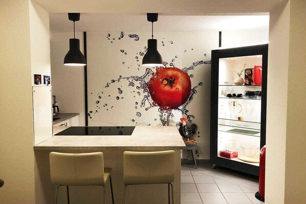 A modern kitchen with a central island, two pendant lights, and a refrigerator with a glass door.