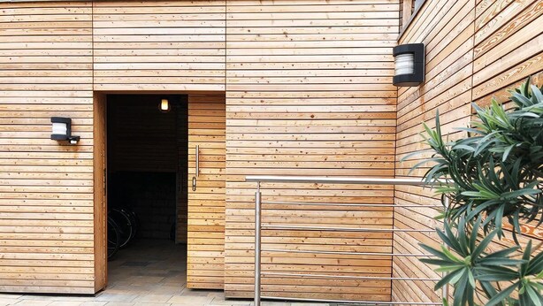 Ein Holzgebäude mit großem offenen Durchgang, einem Metallgitter und einem Blumentopf.