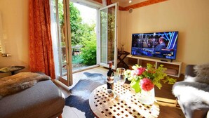 Ein Wohnzimmer mit Fernseher, Tisch, Flasche und Blumen, sowie einer Couch.
