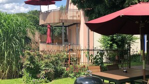 Eine Holzterrasse mit Grill, roten Sonnenschirmen und einem Holztisch.
