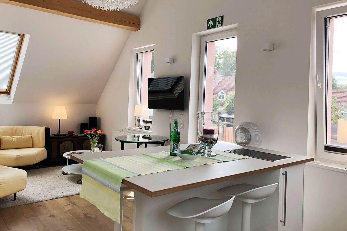 Eine moderne Küche mit Kochinsel, Essbereich mit Tisch und Stühlen sowie Wohnbereich mit Sofa und Lampe.