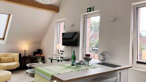 Eine moderne Küche mit Kochinsel, Essbereich mit Tisch und Stühlen sowie Wohnbereich mit Sofa und Lampe.