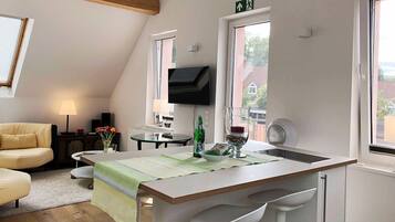 Eine moderne Küche mit Kochinsel, Essbereich mit Tisch und Stühlen sowie Wohnbereich mit Sofa und Lampe.
