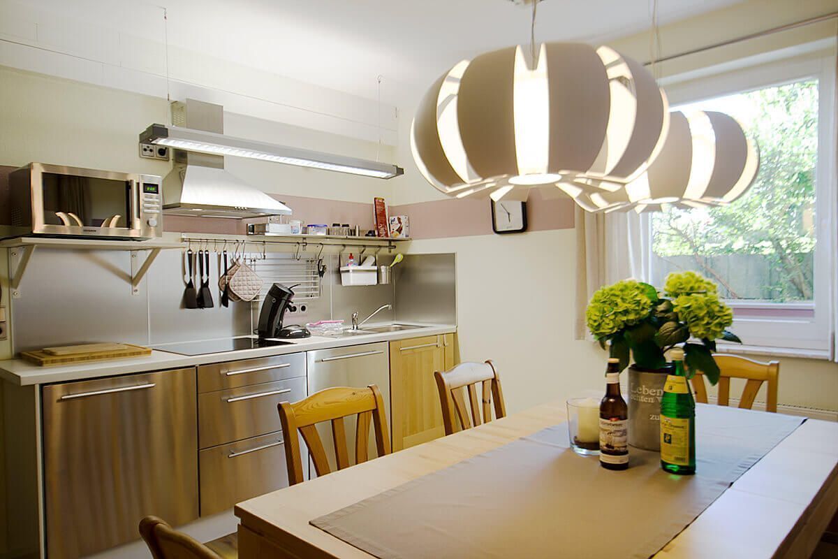Una cocina moderna con electrodomésticos de acero inoxidable, sillas de madera, una mesa de comedor y un ventanal con plantas.