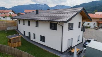 Ein zweigeschossiges Haus mit geneigtem Dach, einem umzäunten Garten und einem Berg im Hintergrund.