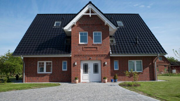 Une maison à deux étages, construite en briques, avec une façade symétrique, une entrée centrale et une allée pavée.