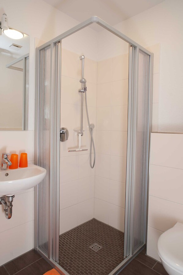 Une douche avec une porte en verre, un lavabo avec un miroir et des toilettes.