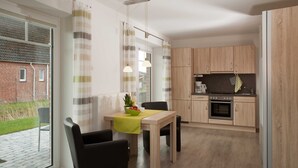 Une cuisine moderne avec des meubles en bois, un coin repas comprenant une table et des chaises, et une vue dégagée sur l’extérieur grâce à une grande fenêtre.