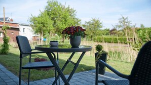 Une terrasse avec une table ronde, deux chaises, une plante en pot et un petit bol.