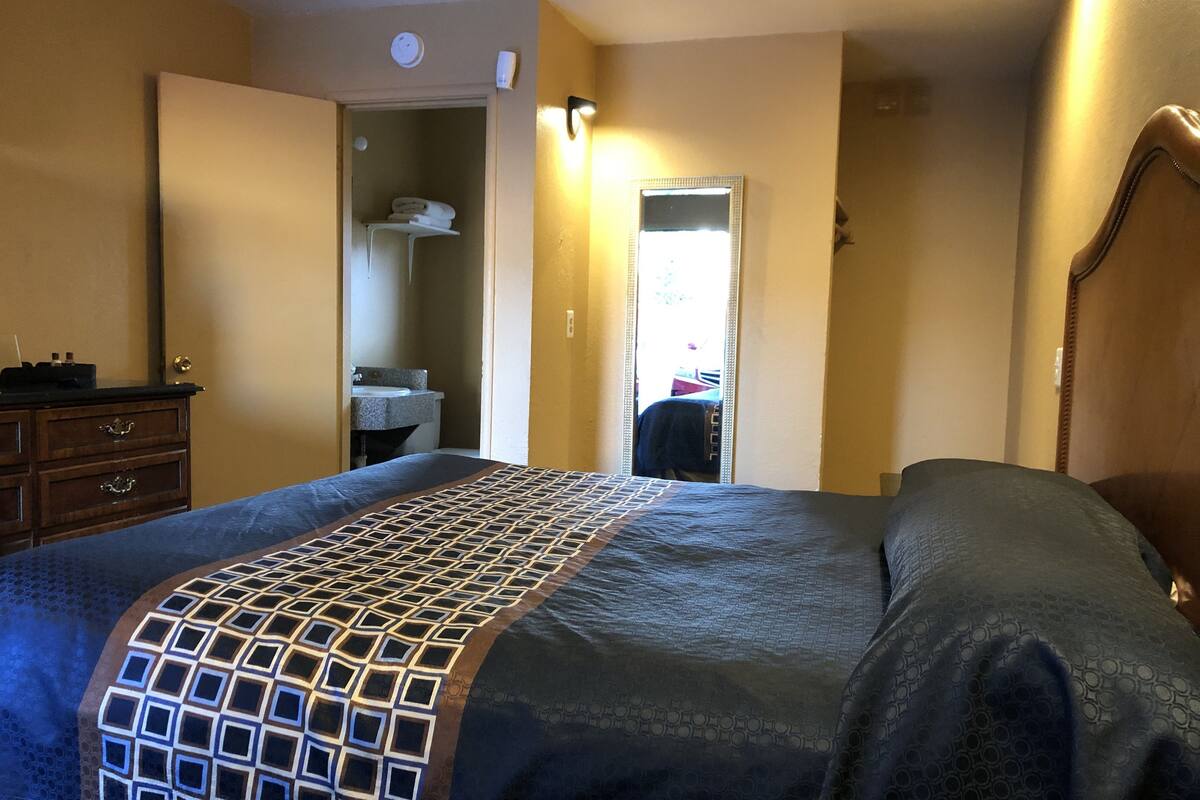 A hotel room with a bed, a dresser, a bathroom visible through an open door, and a nightstand.