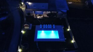 Vista aérea de una propiedad residencial de noche con piscina, un patio cubierto y una casa bien iluminada.