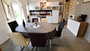 Una cocina compacta con armarios blancos, una estufa y un microondas. Hay una mesa de comedor con sillas y un florero con flores.