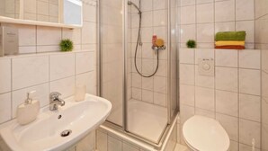 Un baño con ducha de vidrio, lavamanos con espejo e inodoro.