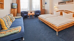 Una habitación de hotel con cama, sofá, una mesita, dos sillas, televisor y armario.
