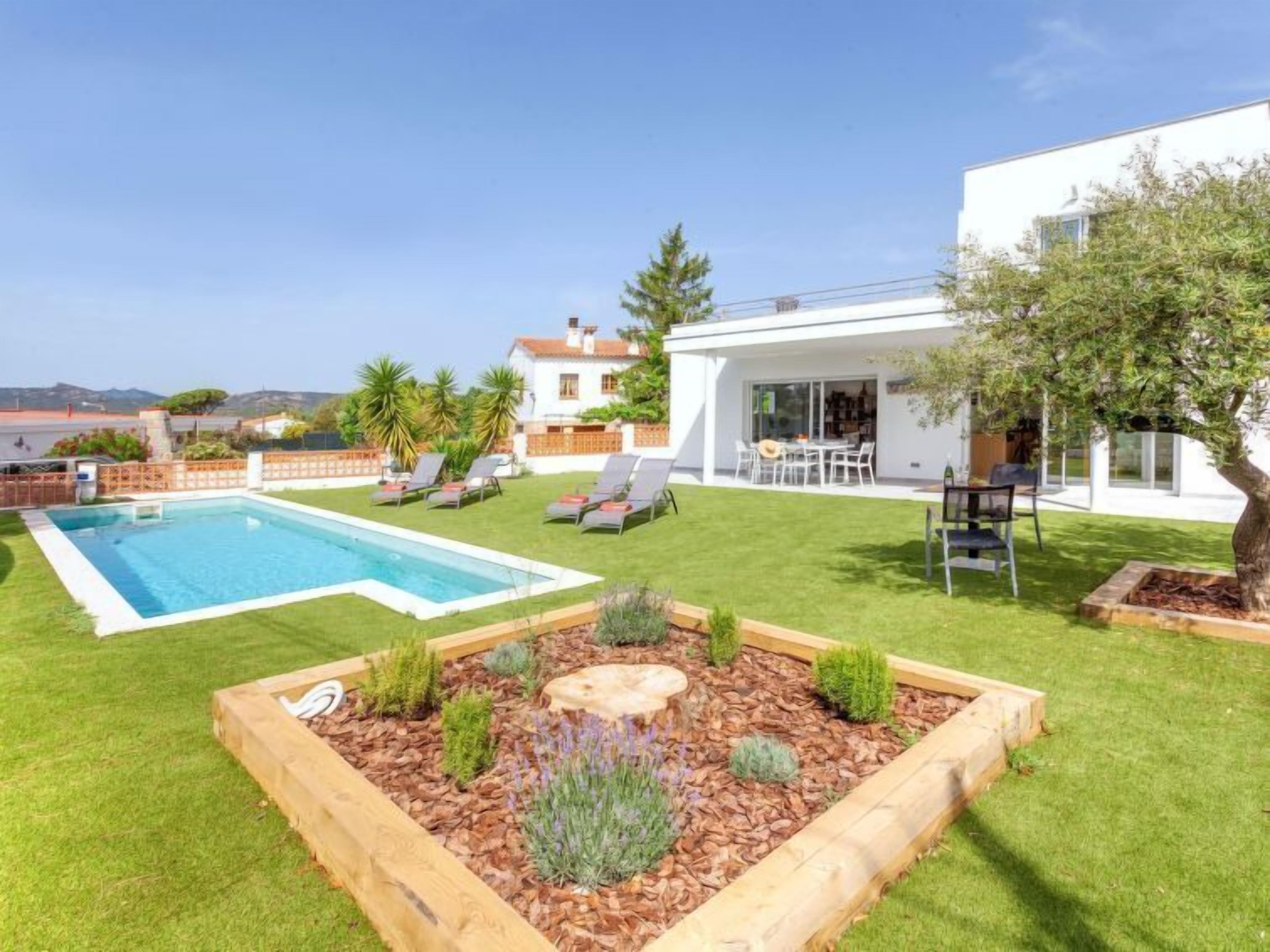 Ein modernes Haus mit Swimmingpool, einer Terrasse mit Liegestühlen und einem gepflegten Garten.